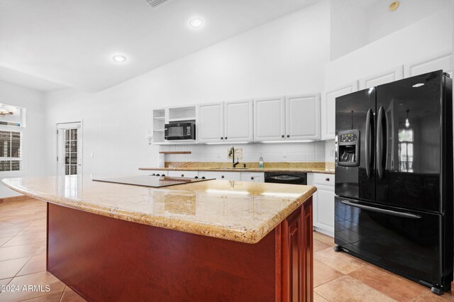 kitchen with light tile patterned floors, backsplash, black appliances, white cabinets, and a kitchen island