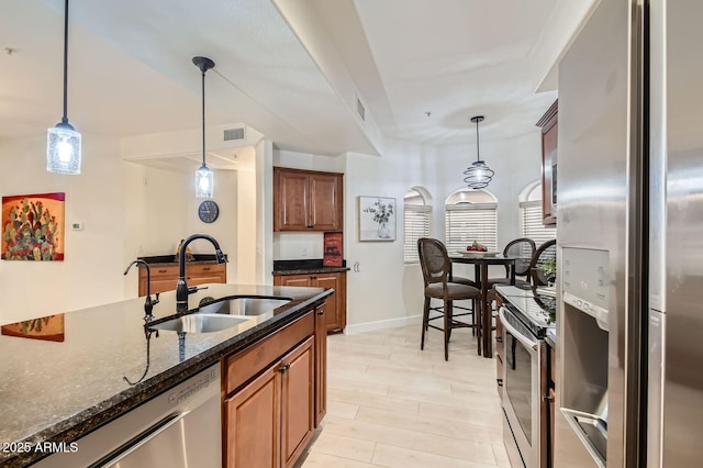 8653 E Royal Palm Rd Unit 1030, Scottsdale, AZ 85258 - kitchen with appliances with stainless steel finishes, dark stone counters, brown cabinetry, and hanging light fixtures
