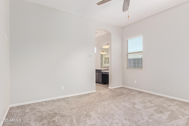 empty room featuring ceiling fan, baseboards, arched walkways, and light colored carpet