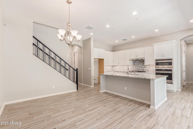 kitchen with double oven, arched walkways, visible vents, and backsplash