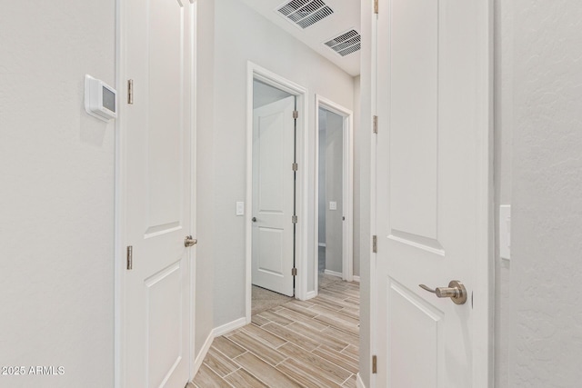 hallway with wood tiled floor, visible vents, and baseboards