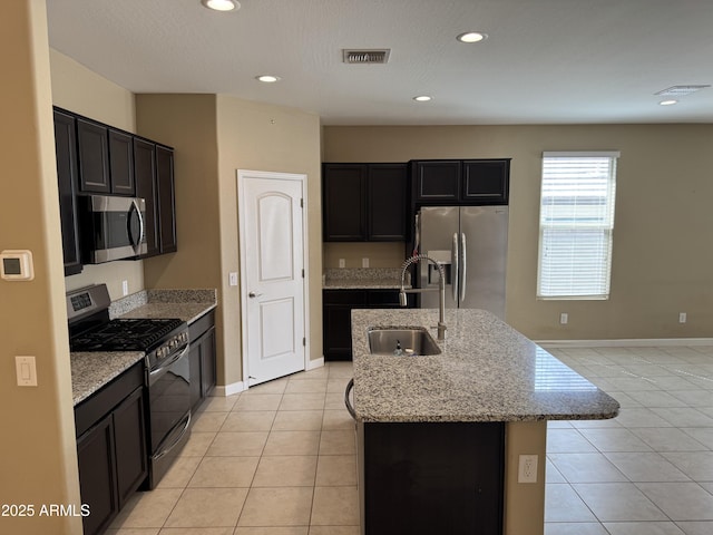 kitchen featuring light stone countertops, appliances with stainless steel finishes, a sink, a kitchen island with sink, and light tile patterned floors