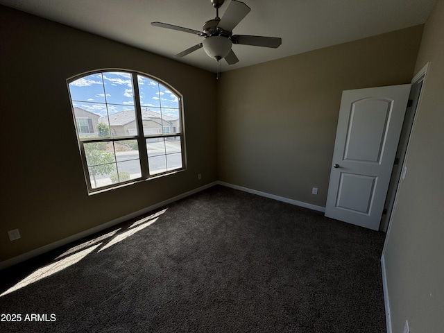 spare room featuring baseboards, a ceiling fan, and dark carpet