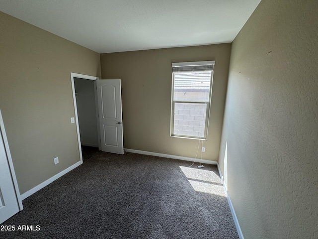 unfurnished room featuring dark colored carpet, baseboards, and a textured wall