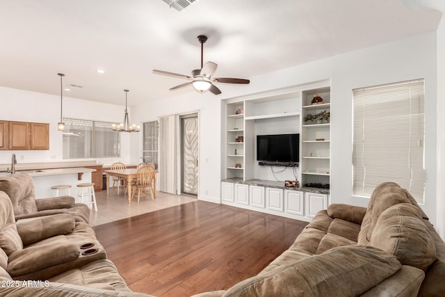 living area featuring built in features, visible vents, recessed lighting, ceiling fan with notable chandelier, and light wood-type flooring