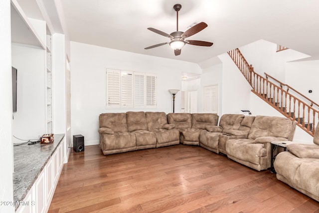 living room with stairway, a ceiling fan, and light wood finished floors