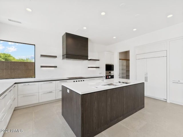 kitchen with dark brown cabinetry, white cabinetry, premium range hood, stovetop, and an island with sink