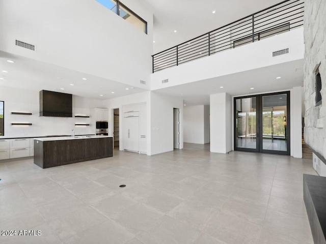 unfurnished living room featuring light tile patterned floors, a towering ceiling, and sink