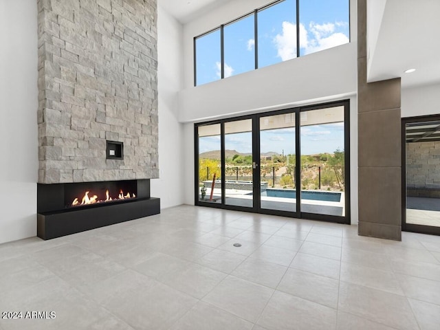 unfurnished living room featuring a high ceiling, light tile patterned floors, and a stone fireplace