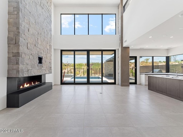 unfurnished living room featuring sink, a towering ceiling, a fireplace, and a wealth of natural light