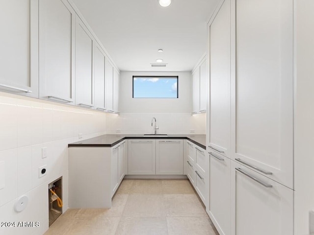 kitchen featuring tasteful backsplash, white cabinetry, sink, and light tile patterned flooring