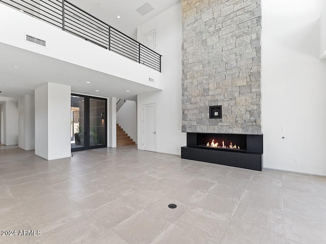 unfurnished living room with light tile patterned flooring, a stone fireplace, and a towering ceiling