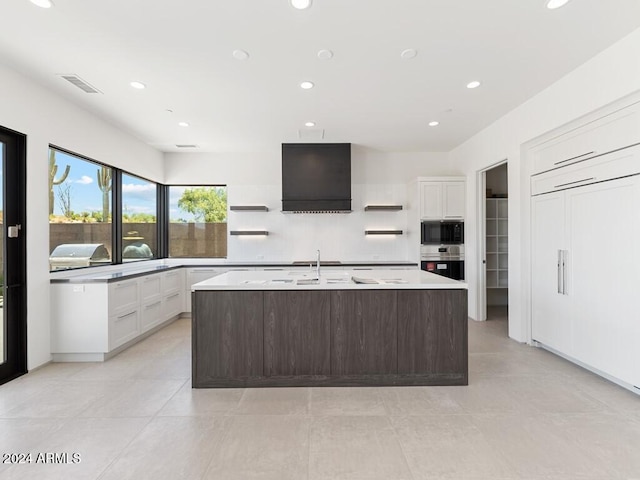 kitchen with double oven, ventilation hood, white cabinetry, and a kitchen island with sink