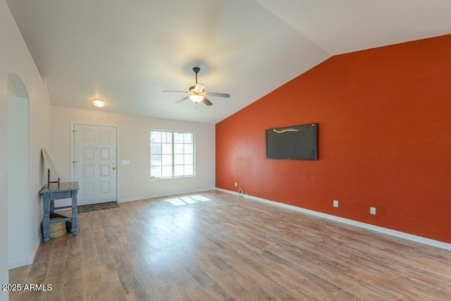 interior space with arched walkways, wood finished floors, a ceiling fan, baseboards, and vaulted ceiling