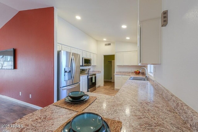 kitchen featuring a sink, visible vents, white cabinets, vaulted ceiling, and appliances with stainless steel finishes