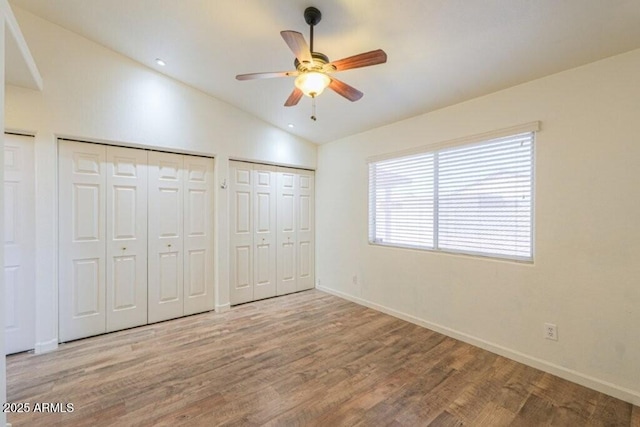 unfurnished bedroom with baseboards, ceiling fan, wood finished floors, vaulted ceiling, and two closets