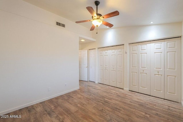 unfurnished bedroom featuring baseboards, visible vents, a ceiling fan, wood finished floors, and multiple closets