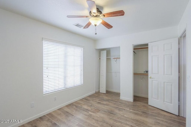 unfurnished bedroom featuring ceiling fan, wood finished floors, visible vents, baseboards, and multiple closets