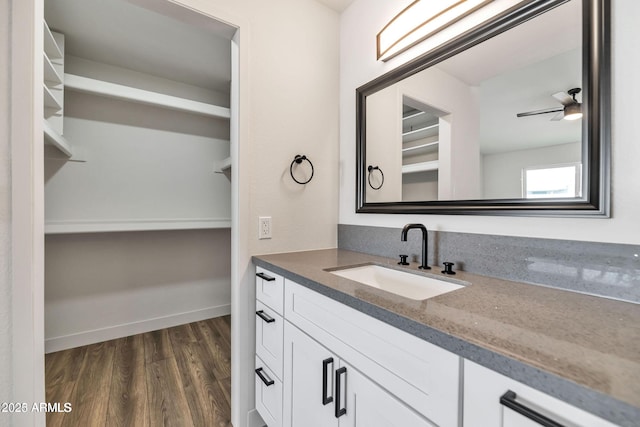 bathroom featuring ceiling fan, wood finished floors, vanity, baseboards, and a walk in closet