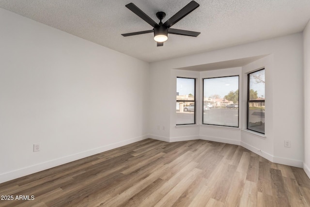 empty room featuring a textured ceiling, ceiling fan, baseboards, and light wood-style floors