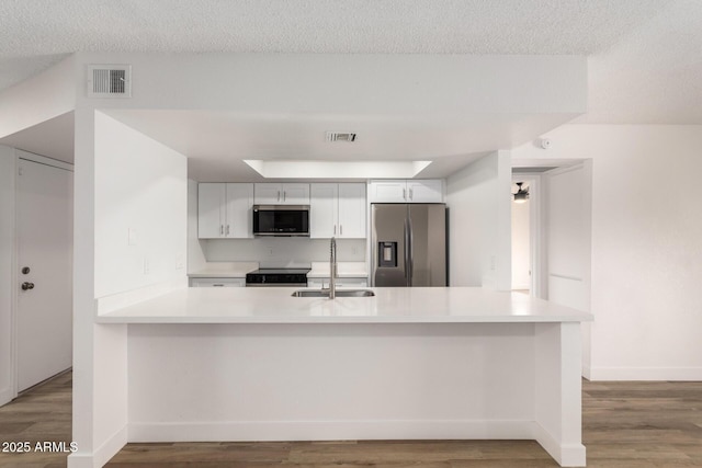 kitchen with white cabinets, a peninsula, appliances with stainless steel finishes, and light countertops