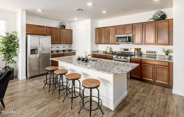 kitchen with a kitchen island with sink, sink, a breakfast bar area, light stone countertops, and stainless steel appliances