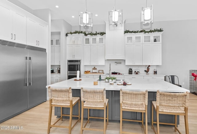 kitchen featuring stainless steel appliances, a spacious island, glass insert cabinets, and white cabinetry