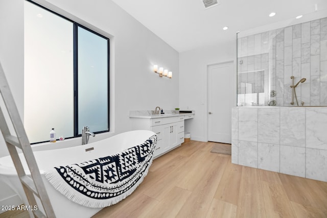 full bath with visible vents, wood finished floors, walk in shower, a freestanding bath, and vanity