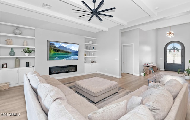 living room featuring built in shelves, visible vents, a glass covered fireplace, beamed ceiling, and baseboards