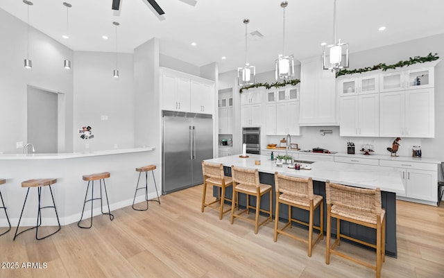 kitchen featuring white cabinets, glass insert cabinets, appliances with stainless steel finishes, decorative light fixtures, and a kitchen bar