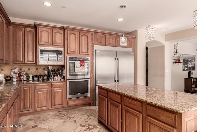 kitchen with built in appliances, tasteful backsplash, hanging light fixtures, light stone countertops, and a kitchen island