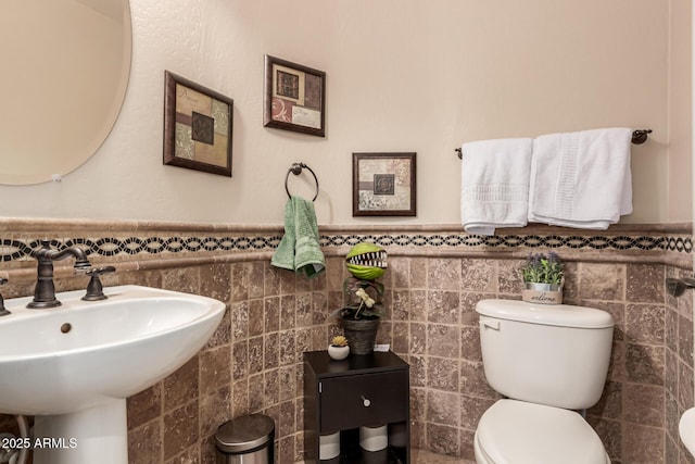 bathroom featuring toilet, tile walls, and sink