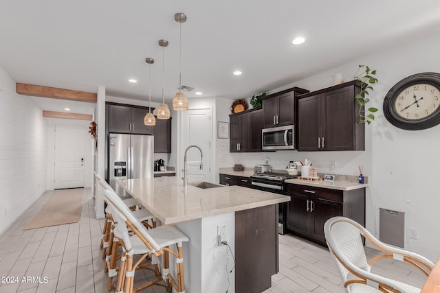 kitchen with sink, light stone counters, a center island with sink, appliances with stainless steel finishes, and pendant lighting