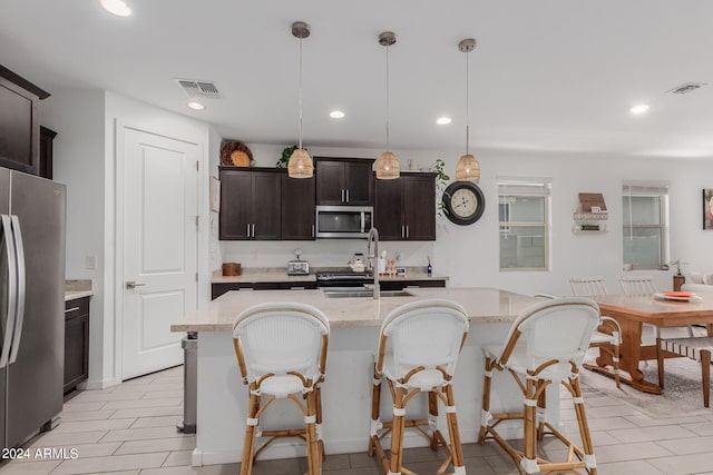 kitchen with appliances with stainless steel finishes, decorative light fixtures, a breakfast bar, and a center island with sink