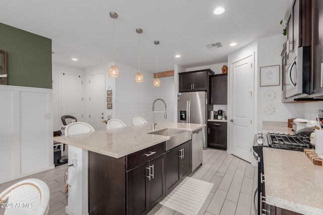 kitchen featuring sink, appliances with stainless steel finishes, hanging light fixtures, dark brown cabinetry, and an island with sink