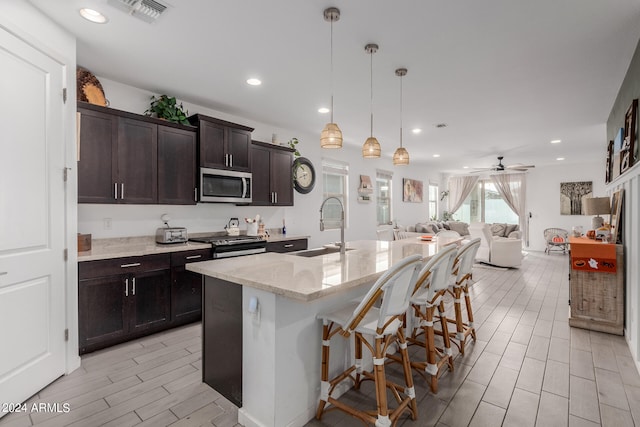 kitchen with sink, a kitchen bar, hanging light fixtures, a kitchen island with sink, and stainless steel appliances