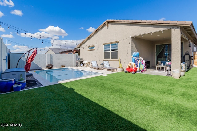 rear view of house featuring a fenced in pool, a lawn, and a patio