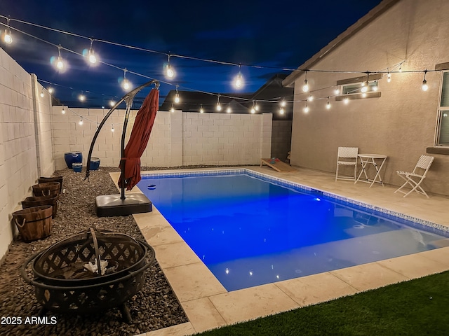 pool at night featuring an outdoor fire pit and a patio area