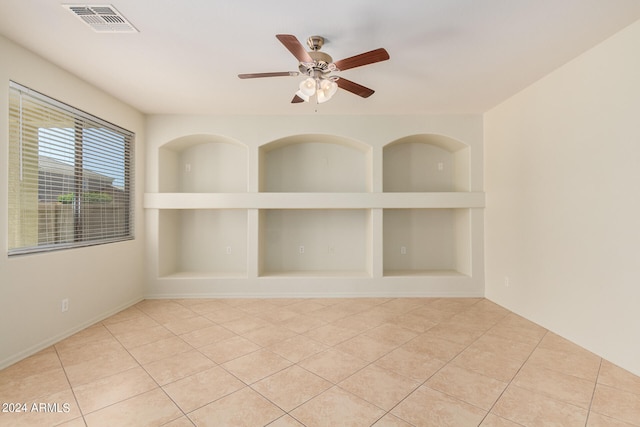 empty room with built in features, ceiling fan, and light tile floors