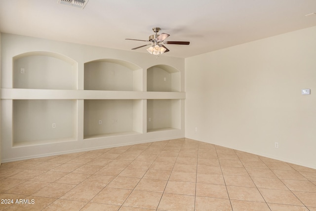 tiled spare room featuring built in shelves and ceiling fan