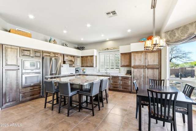 kitchen featuring decorative light fixtures, stainless steel appliances, a kitchen island, backsplash, and sink