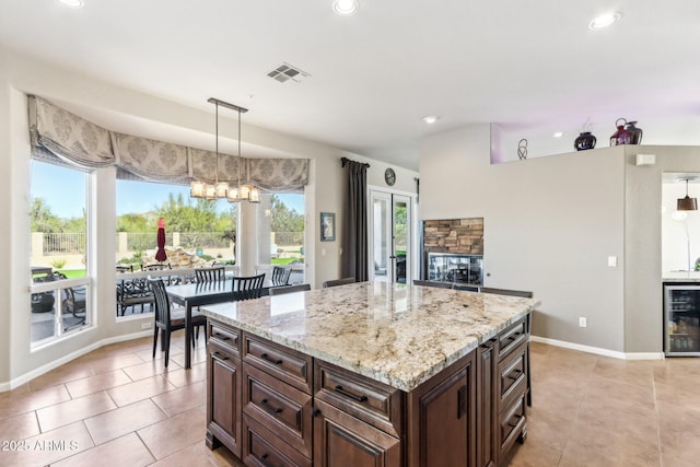 kitchen with light stone countertops, a center island, decorative light fixtures, light tile patterned floors, and wine cooler