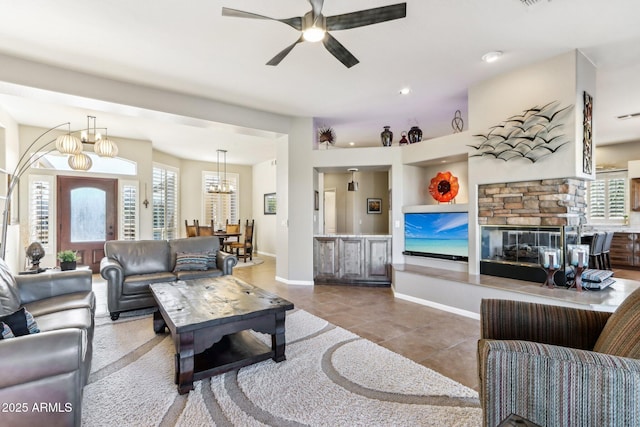 tiled living room featuring a stone fireplace and ceiling fan with notable chandelier