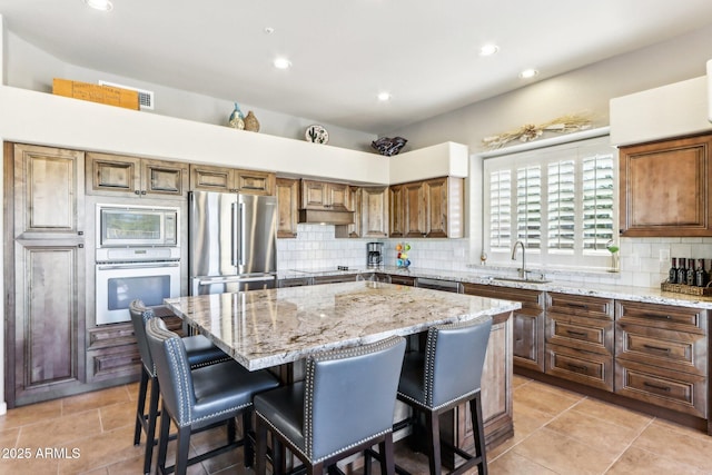 kitchen featuring stainless steel appliances, sink, a center island, light stone counters, and a breakfast bar area