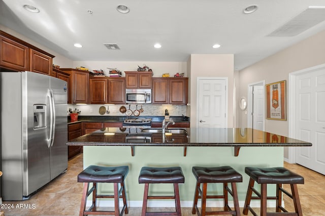 kitchen featuring appliances with stainless steel finishes, an island with sink, tasteful backsplash, a breakfast bar, and sink