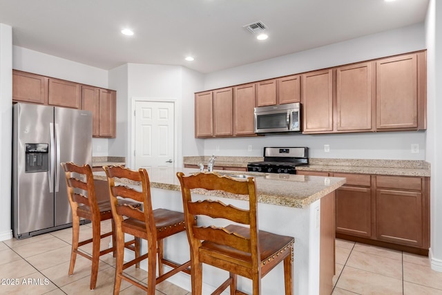 kitchen featuring stainless steel appliances, a kitchen island with sink, visible vents, and a breakfast bar area