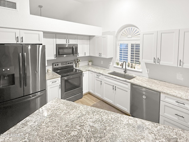 kitchen with stainless steel appliances, white cabinetry, light stone countertops, and sink