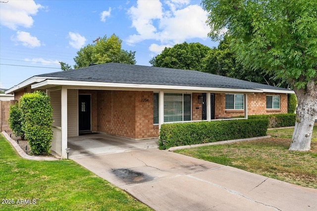 single story home featuring brick siding, an attached carport, a front yard, roof with shingles, and driveway