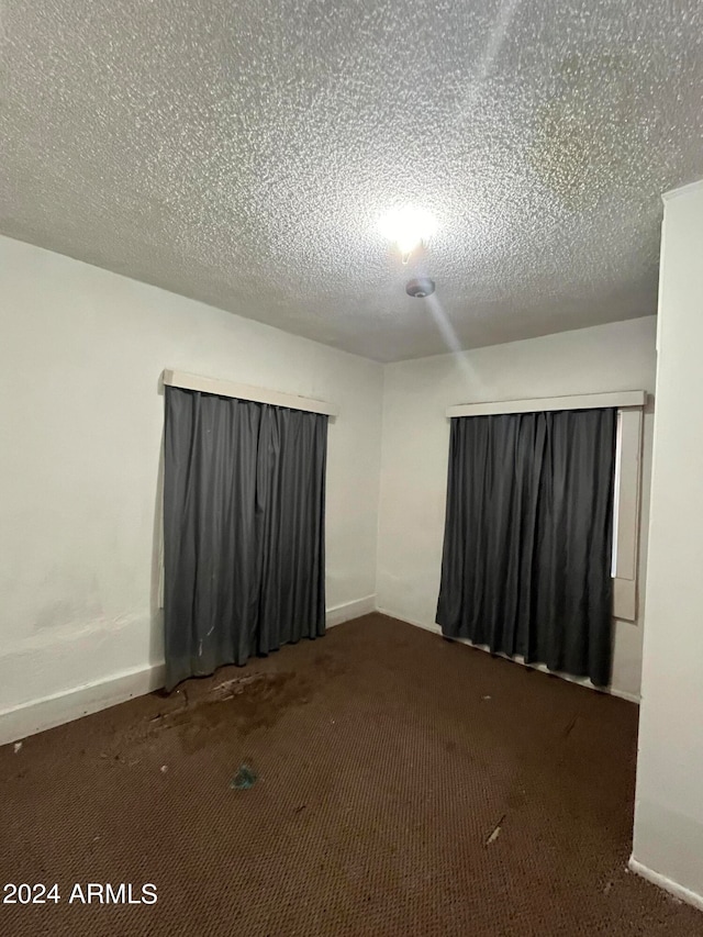 additional living space featuring a textured ceiling and dark carpet