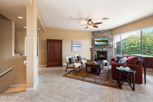 living room with a stone fireplace, ceiling fan, and light parquet floors